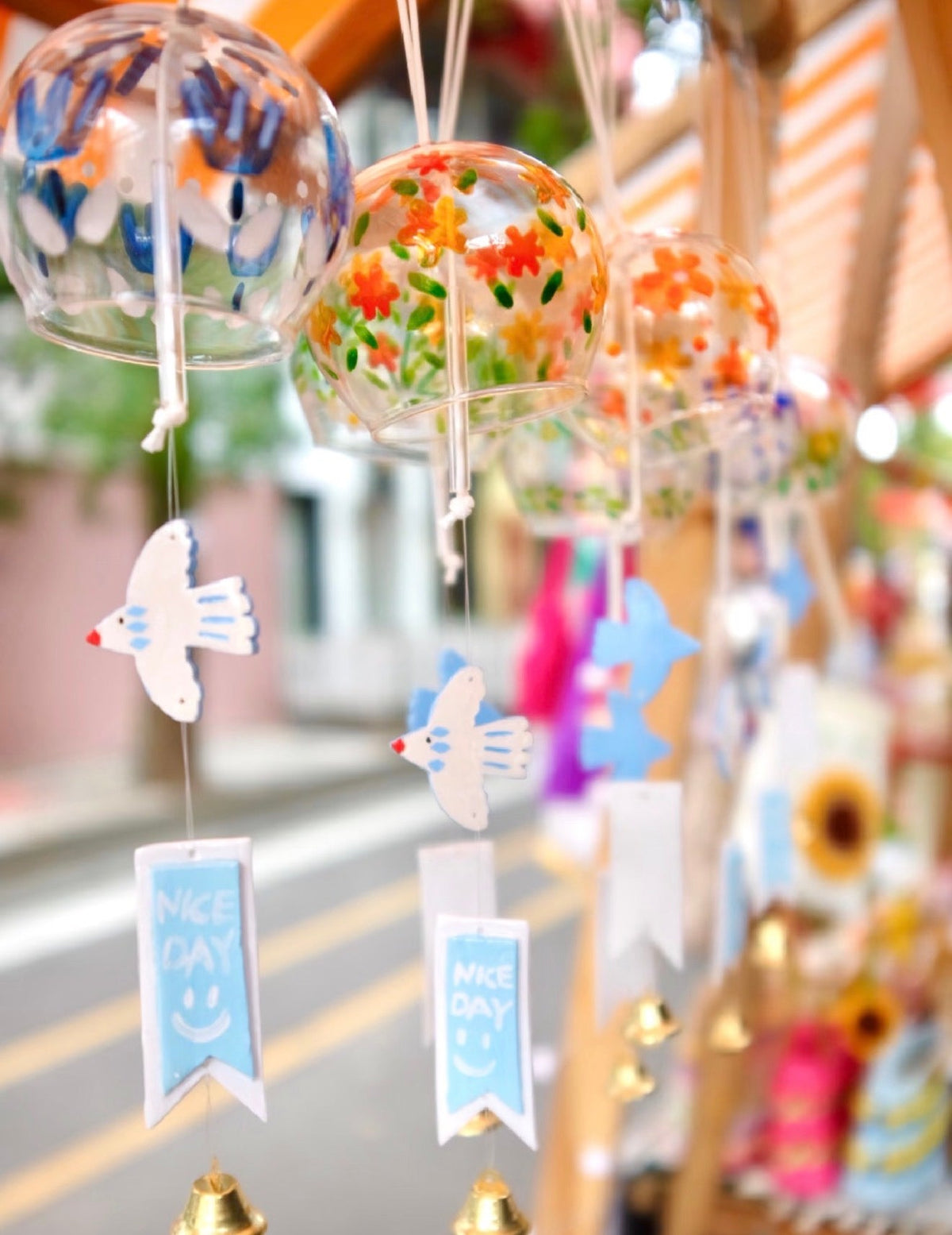 Colorful Japanese glass furin wind chimes with floral designs and bird ornaments hanging outdoors