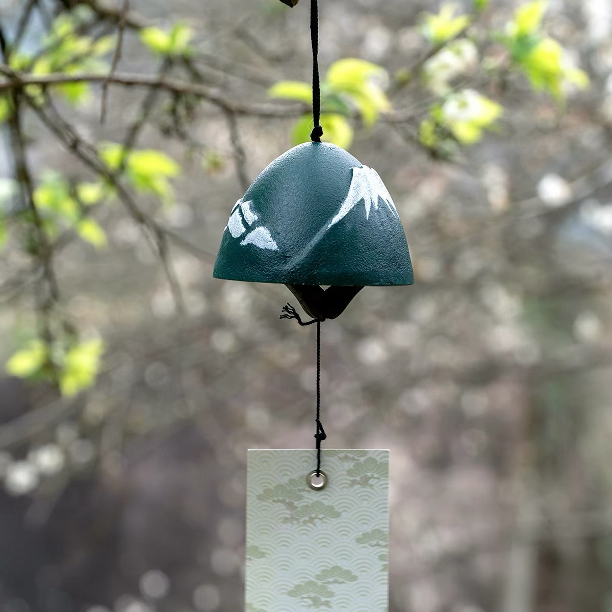Handcrafted dark green Mount Fuji cast iron furin wind chime hanging outdoors with a decorative tanzaku tag.