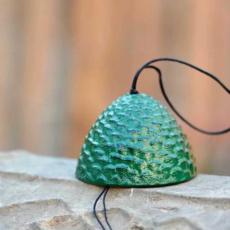 Japanese green cast iron pine cone wind chime displayed on a stone surface