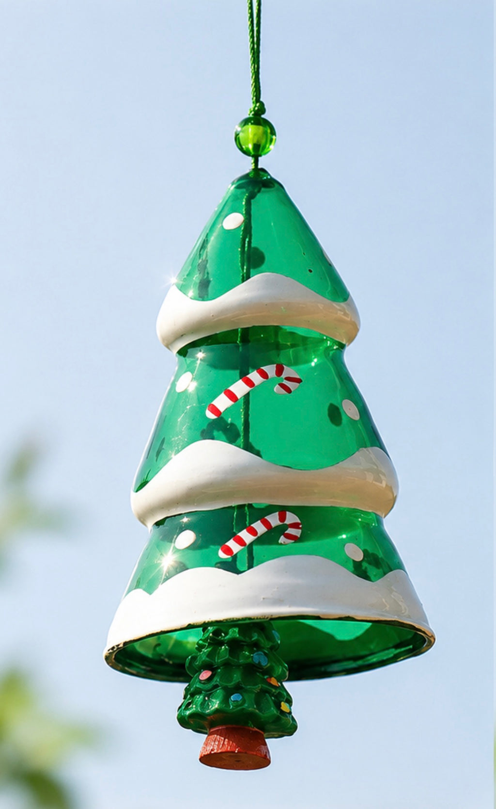 Close-up of a green Christmas tree glass wind chime with snow and candy cane details