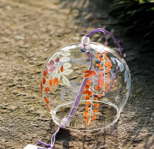 Japanese glass furin wind chime with orange wisteria floral design displayed on a stone surface
