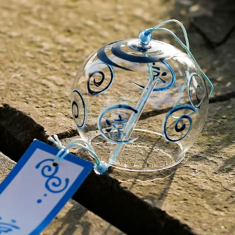 Japanese glass furin wind chime with blue swirl pattern and tanzaku strip displayed on a stone surface