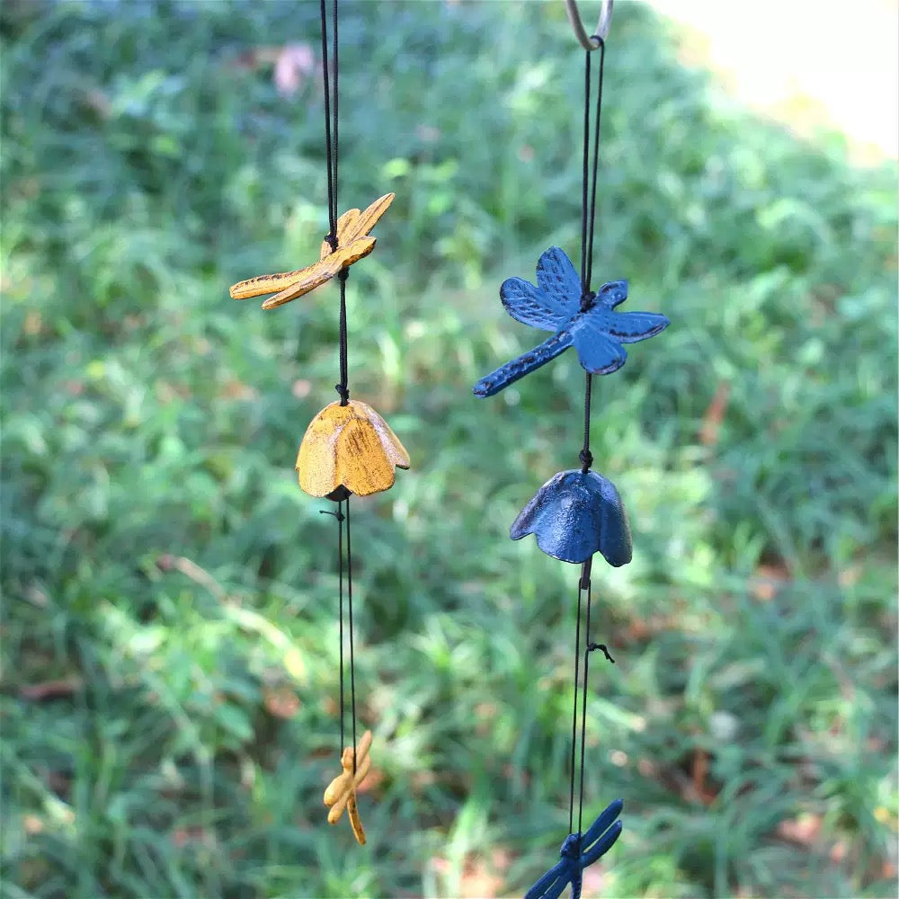 Blue and yellow dragonfly cast iron wind chimes hanging in a peaceful outdoor garden setting