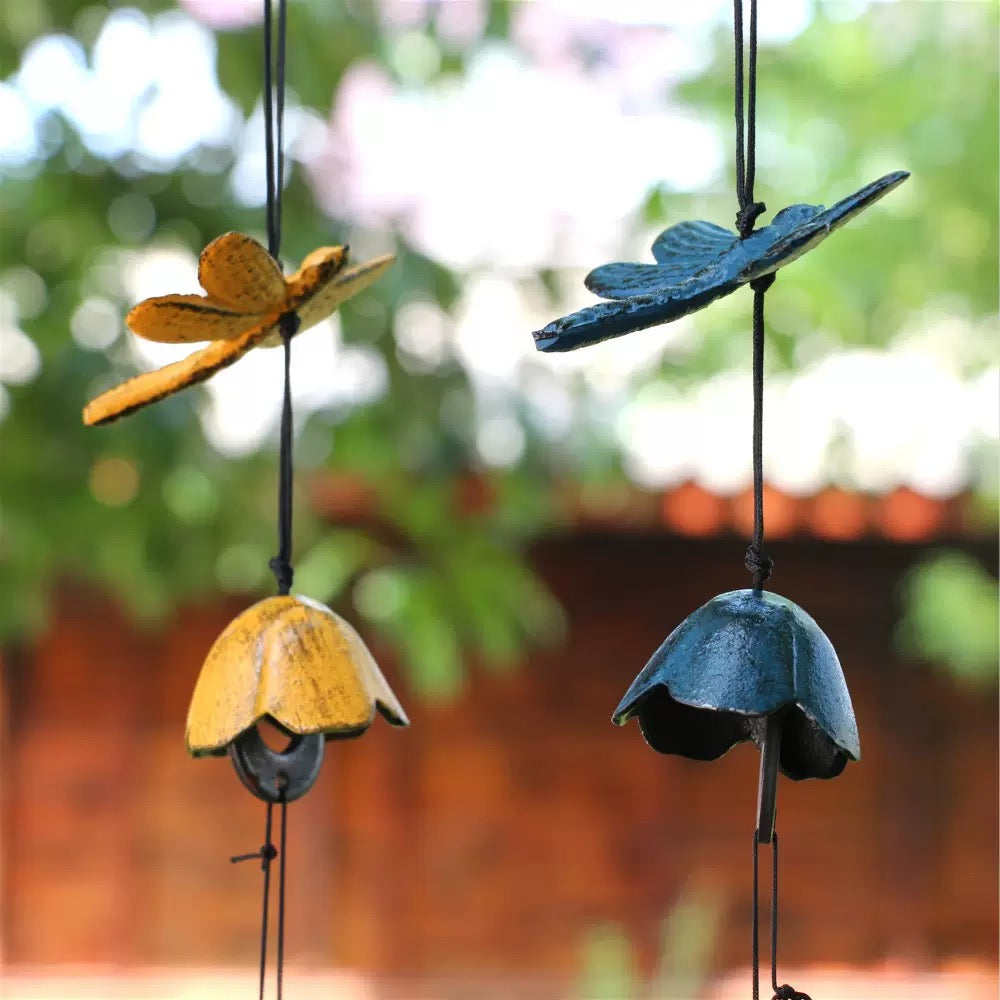 Blue and yellow dragonfly cast iron wind chimes hanging outdoors with a warm wooden garden background