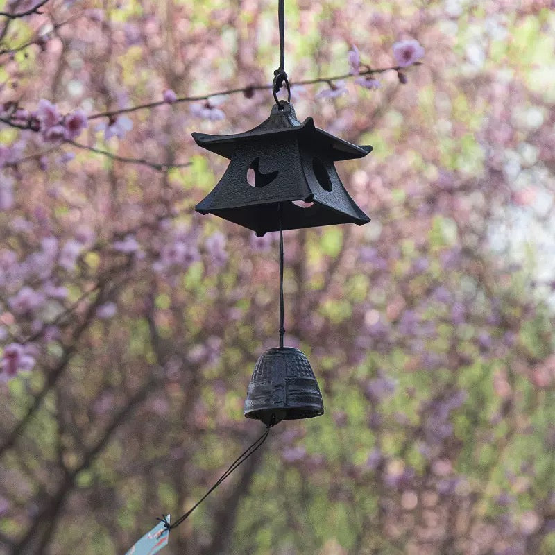 Japanese black cast iron pagoda furin wind chime hanging outdoors with purple blossoms
