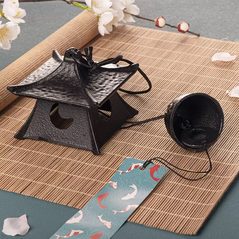 Japanese cast iron temple pagoda wind chime displayed on a bamboo mat with floral decor