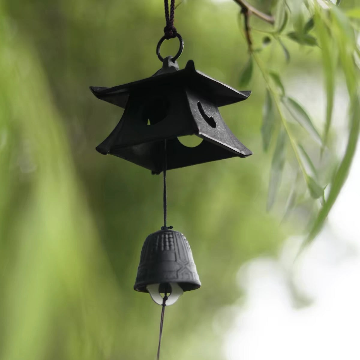 Japanese black cast iron pagoda wind chime hanging among soft green willow leaves