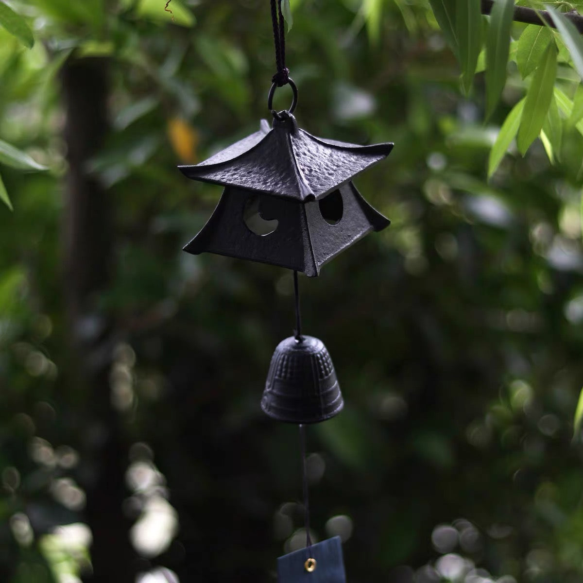 Japanese black cast iron pagoda wind chime hanging in a shaded garden setting