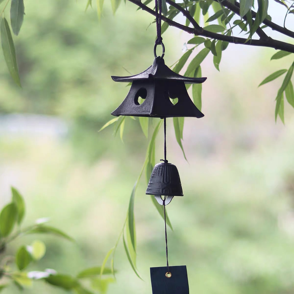 Japanese black cast iron temple pagoda furin wind chime hanging outdoors in a peaceful garden