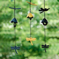 Assorted dragonfly cast iron wind chimes in blue, yellow, and dark green hanging in a garden