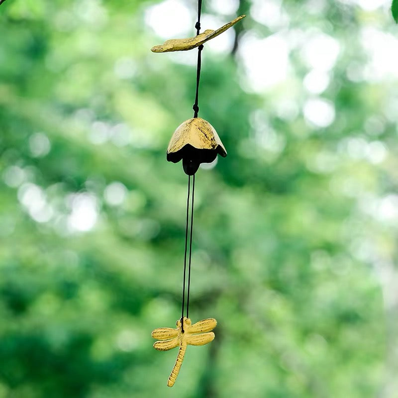 Yellow dragonfly cast iron wind chime hanging outdoors with a soft green garden background
