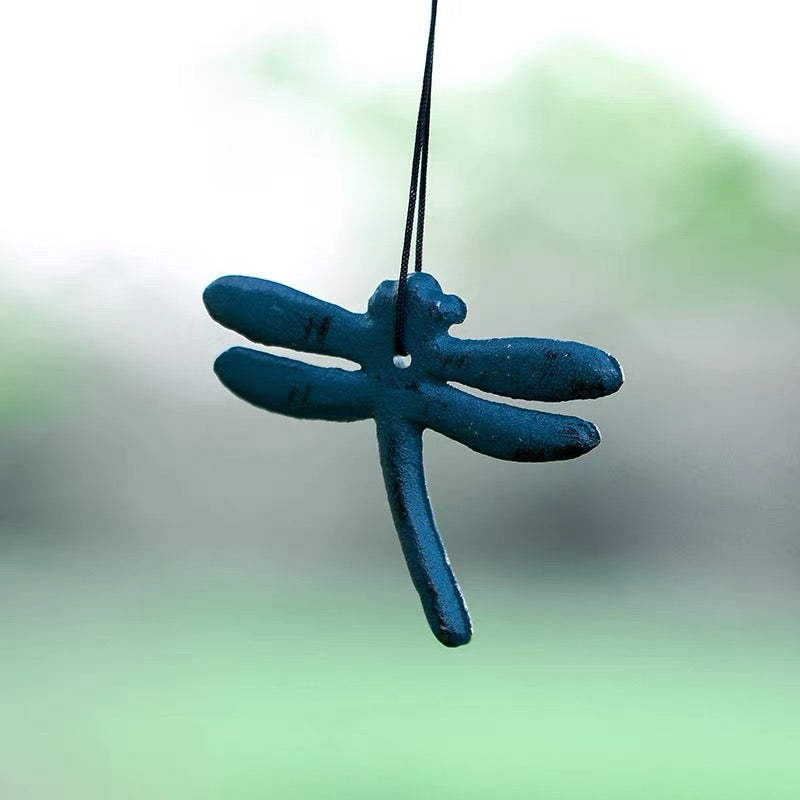Blue dragonfly cast iron wind chime hanging with a soft green garden background