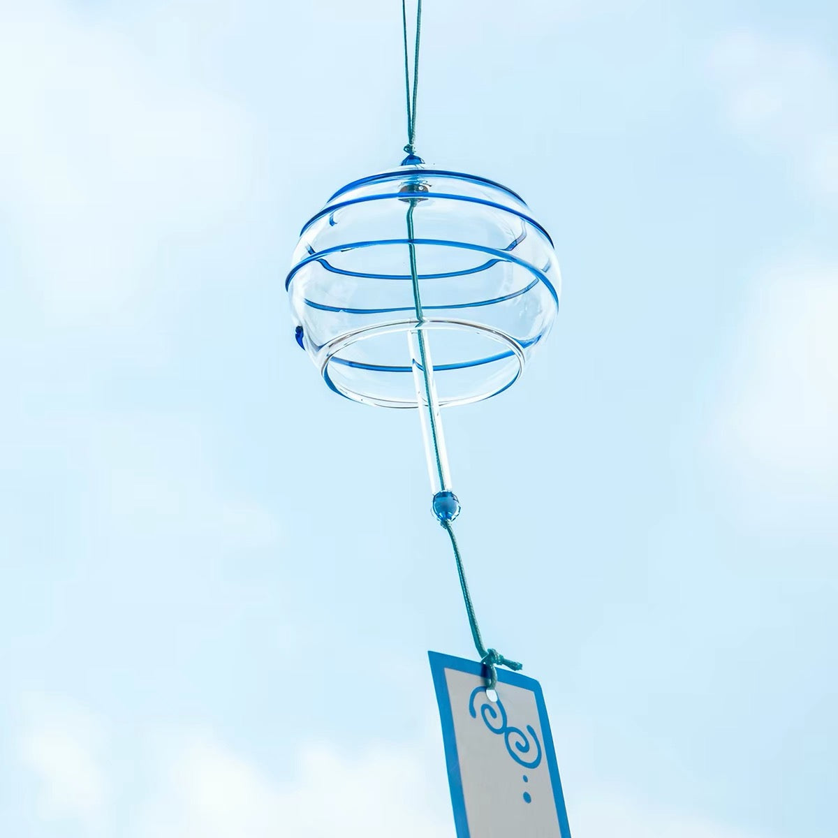 Japanese glass furin wind chime with blue cool breeze design and tanzaku strip hanging against a soft sky background