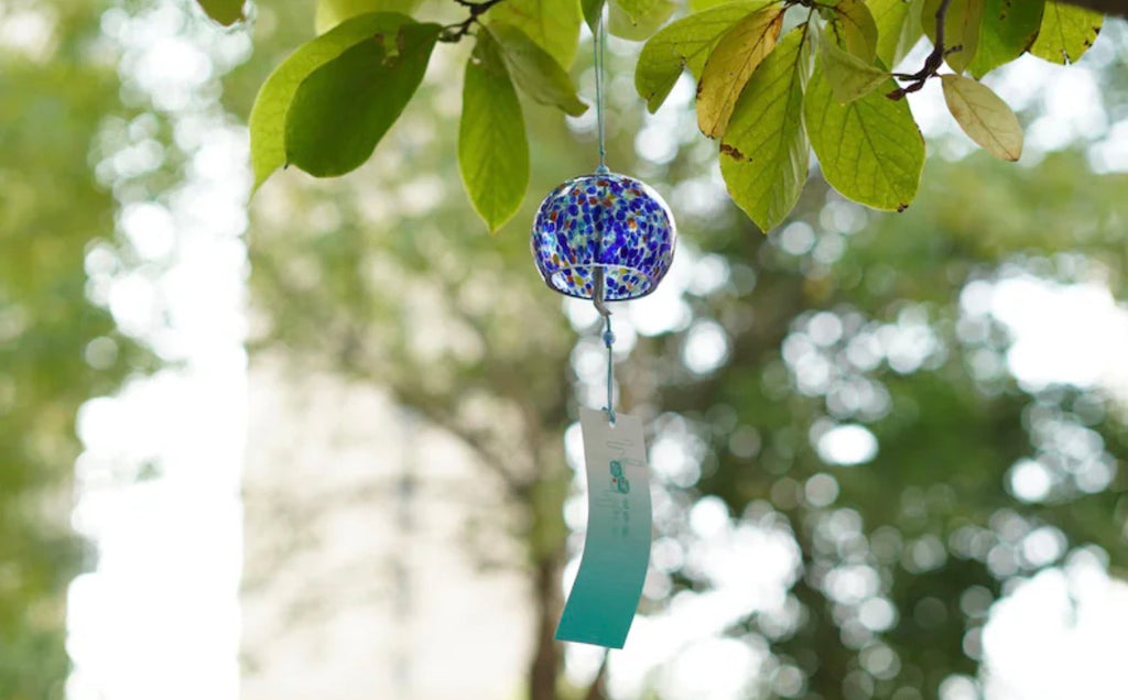 Blue mosaic Japanese glass furin wind chime hanging from a leafy tree outdoors