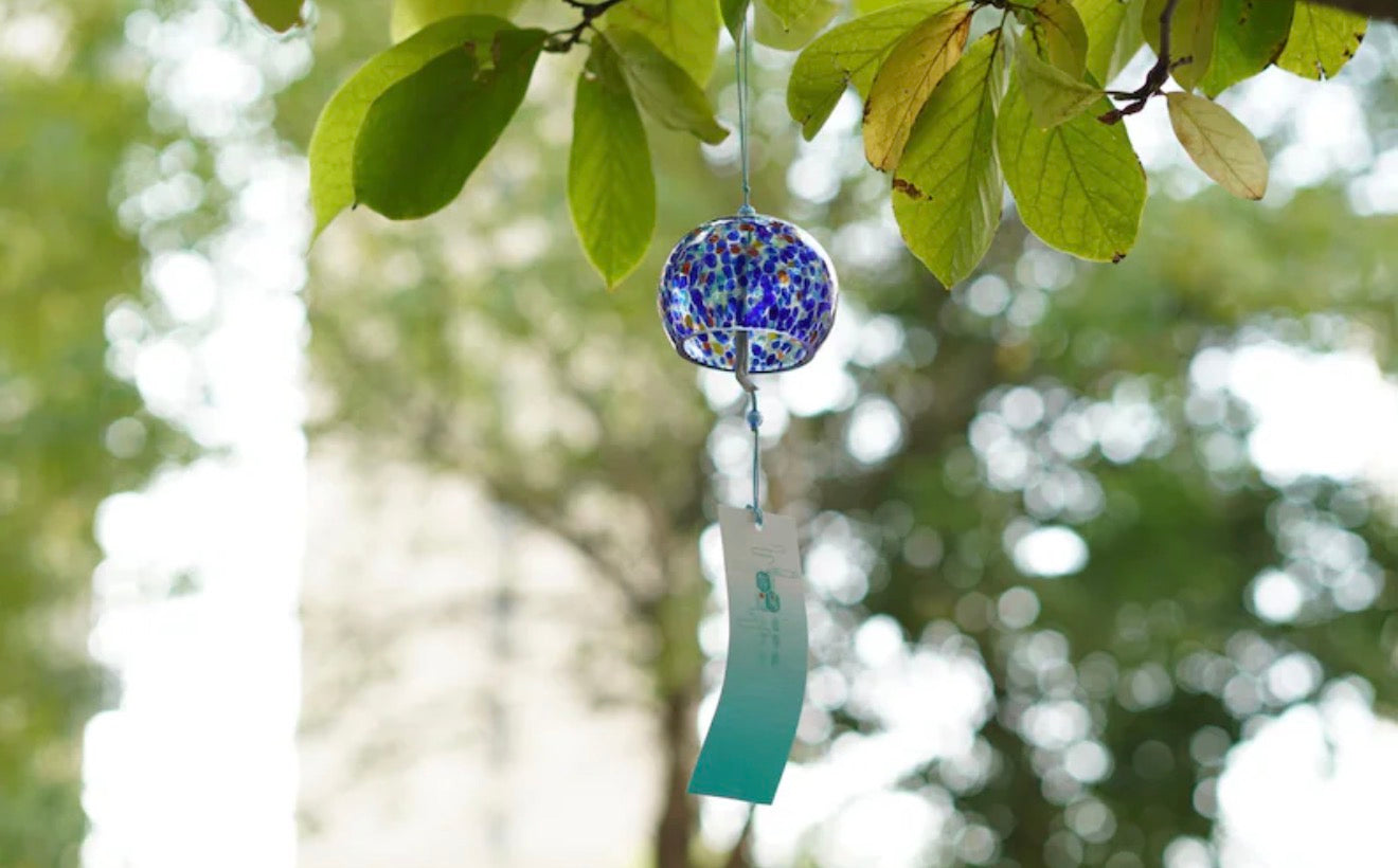 Blue mosaic Japanese glass furin wind chime hanging from a leafy tree outdoors