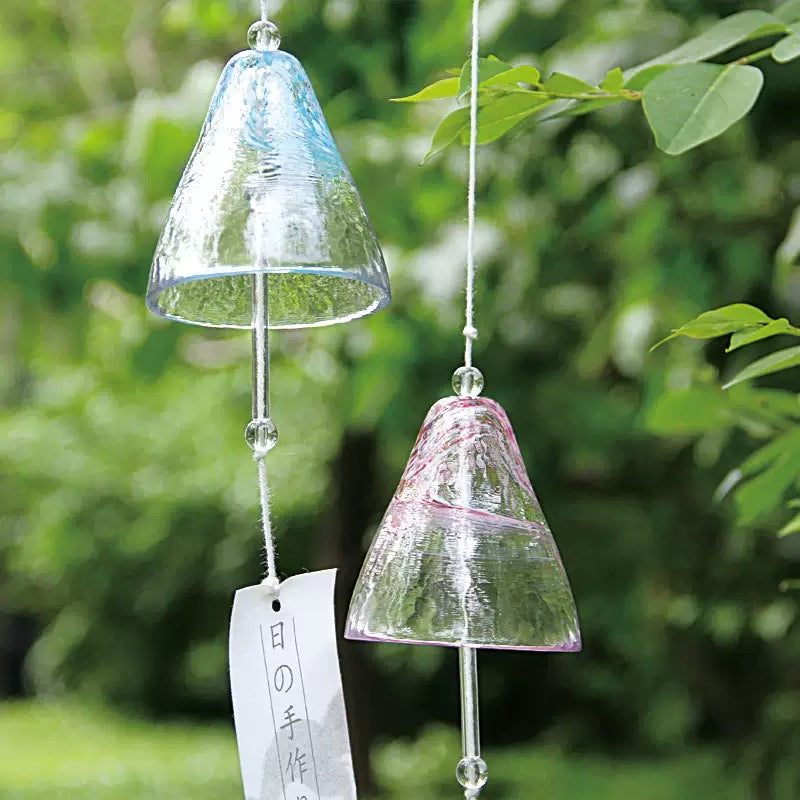 Blue and pink Japanese handmade thick glass furin wind chimes hanging in a sunny green garden with tanzaku paper strips.