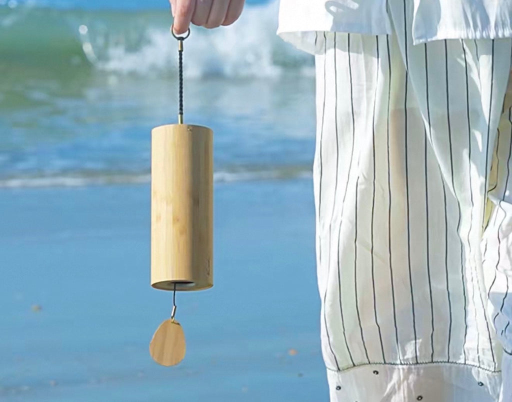 Hand holding a Japanese bamboo meditation wind chime by the sea, showing its natural bamboo design.