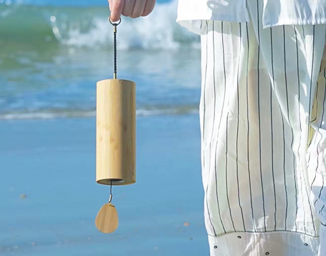 Hand holding a Japanese bamboo meditation wind chime by the sea, showing its natural bamboo design.