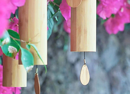 Japanese bamboo meditation wind chimes hanging among bright pink flowers, creating a calm Zen garden decor scene.