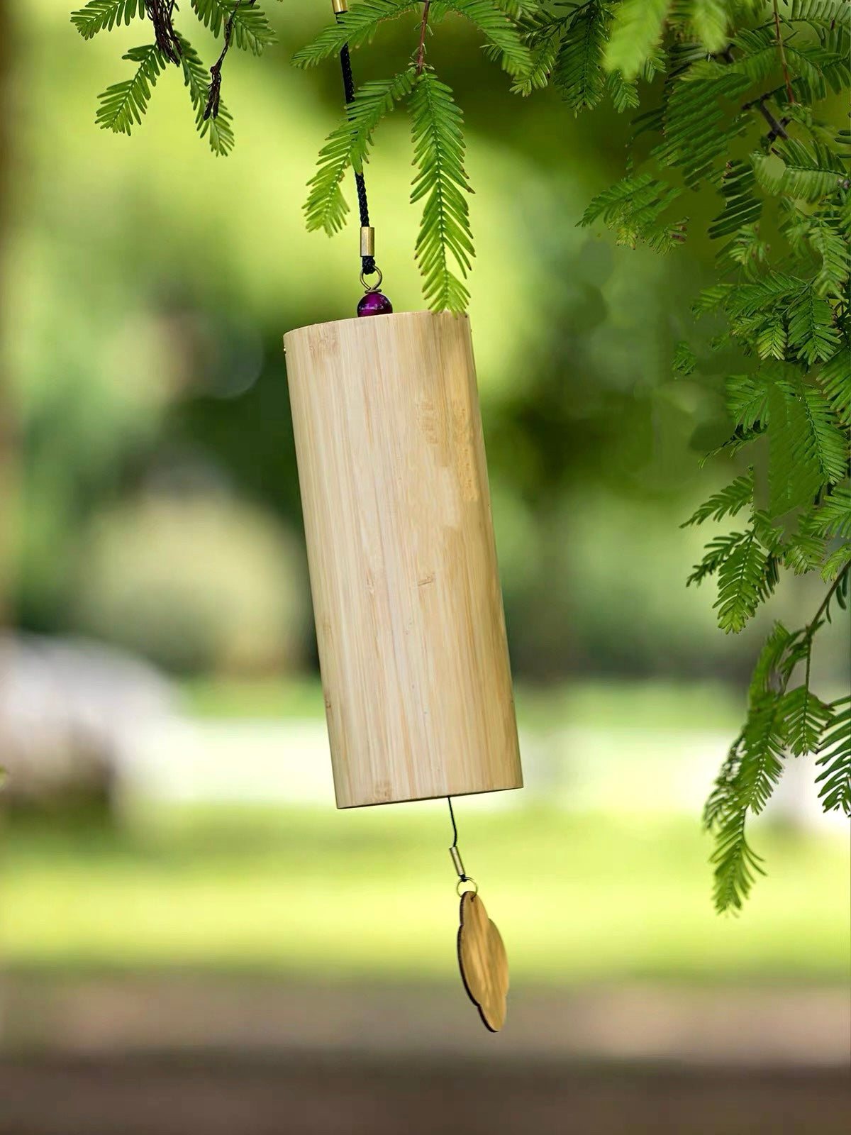 Japanese bamboo meditation wind chime hanging outdoors among green leaves in a peaceful garden setting.