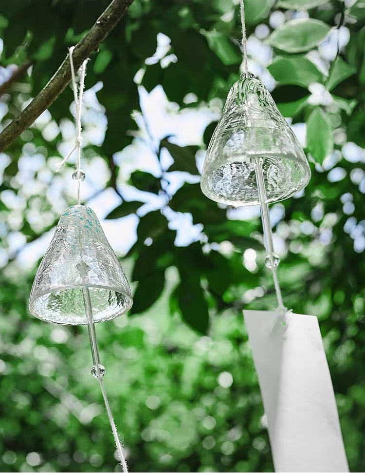 Two Japanese handmade thick glass wind chimes hanging from tree branches in a lush green garden.