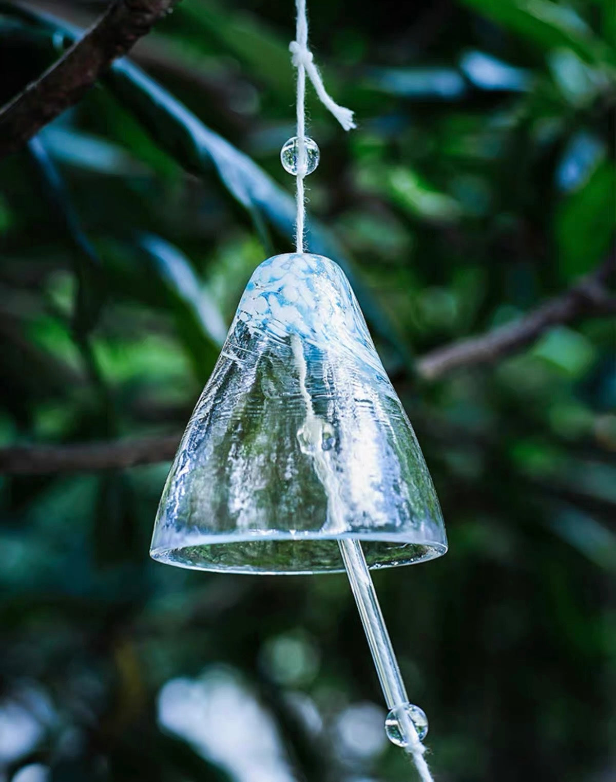 Close-up of a blue Japanese handmade thick glass furin wind chime hanging among green leaves.