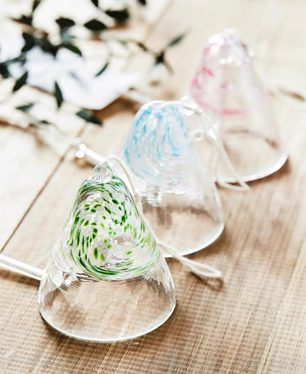 Japanese handmade thick glass wind chimes in green, blue, and pink displayed on a wooden surface.