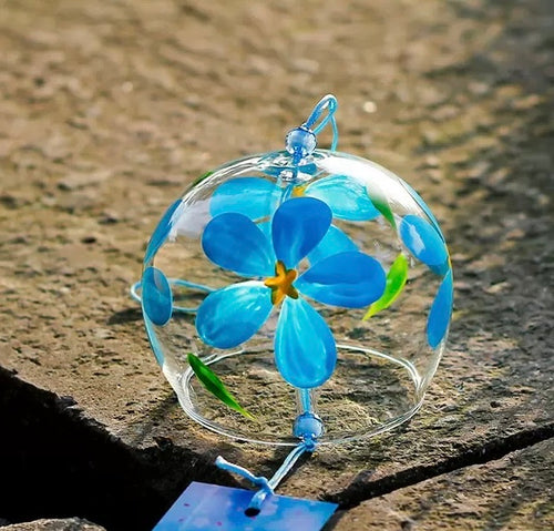 Japanese glass furin wind chime with blue flower design displayed on a stone surface